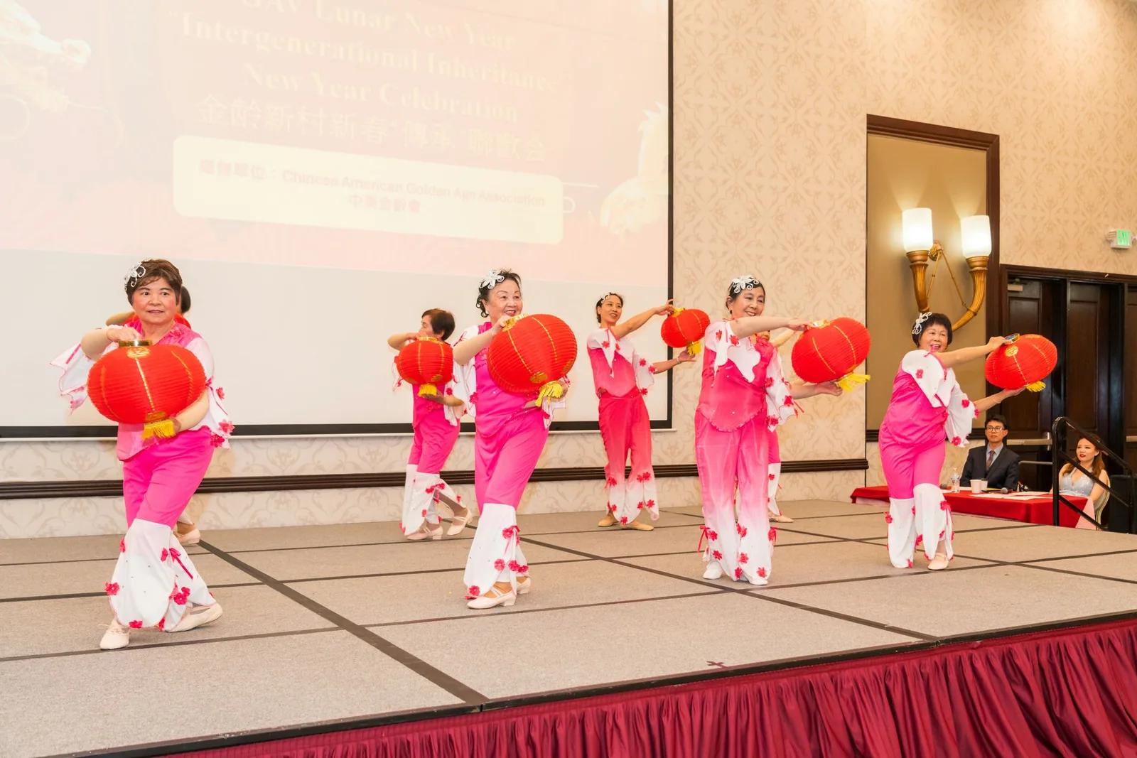 Senior performers in pink costumes dancing with red lanterns on stage at a New Year celebration