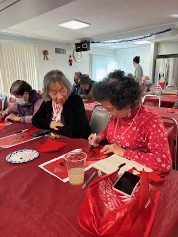 Two residents writing "Fu" characters together in the activity room
