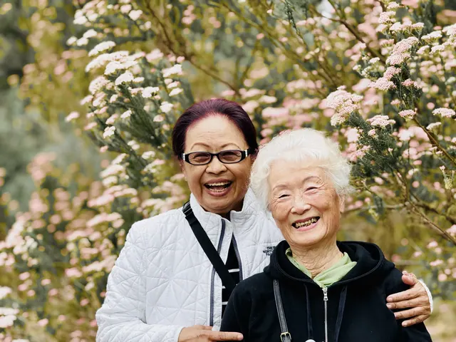 Two seniors smiling together in front of pink blossoms