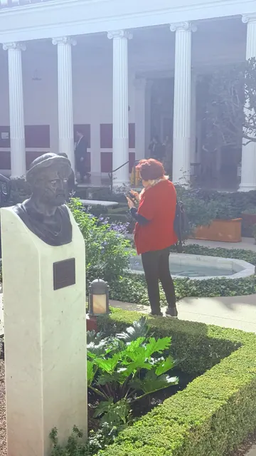 A visitor taking photos beside a bronze bust and reflecting pool in the museum garden courtyard