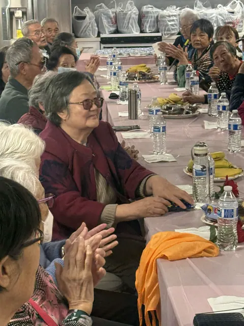 Residents clapping at tables set with fruit, bottled water, and snacks
