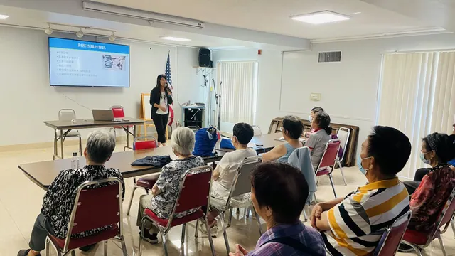 A presenter uses slides to address seated seniors at the fraud prevention seminar