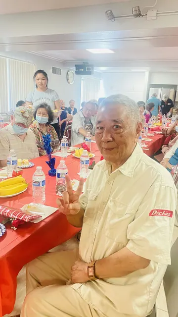 A senior smiles and flashes a victory sign at the birthday party table
