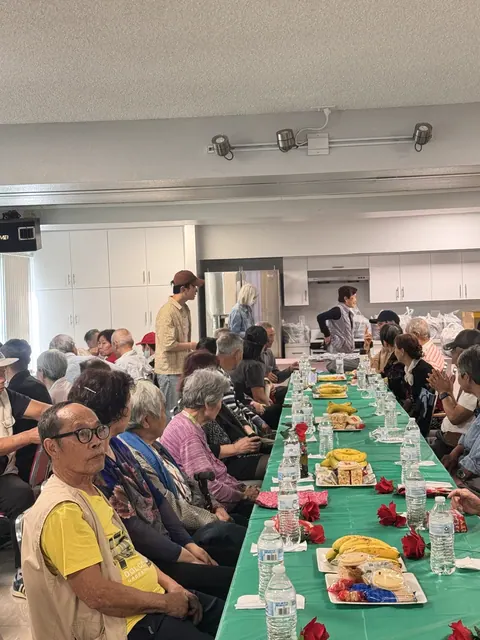 Residents seated along a long table with roses, bananas, and refreshments
