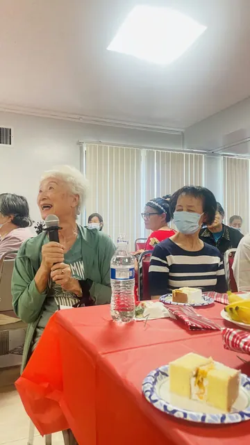 A senior speaks into a microphone at the birthday party, with cake served on the table