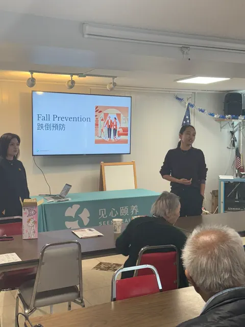Speakers presenting a fall prevention seminar to residents, with a "Fall Prevention" slide on screen