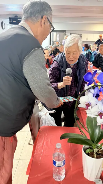 A birthday celebrant speaking into a microphone while receiving a gift
