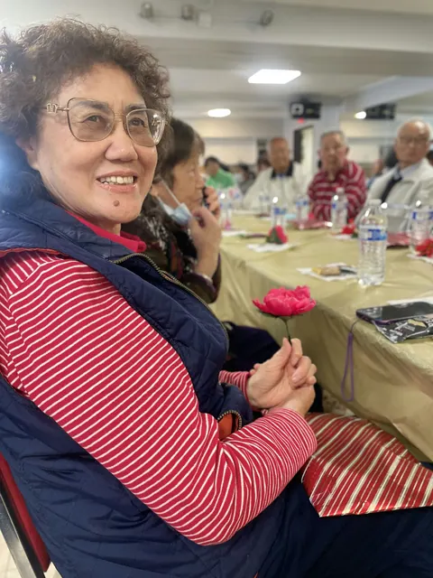 A resident smiling and holding a red flower at the birthday party