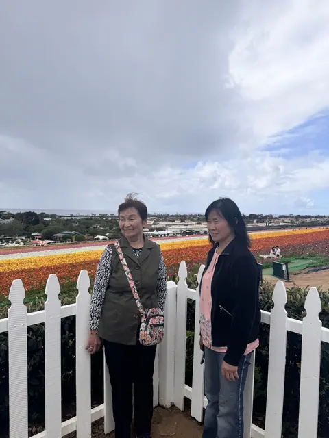 Two residents by a white picket fence with the colorful flower fields and coastline behind