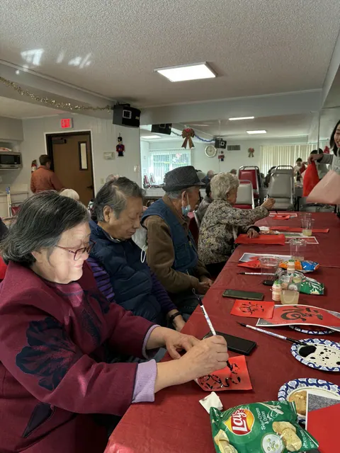 Residents seated at a long table writing "Fu" characters on red paper