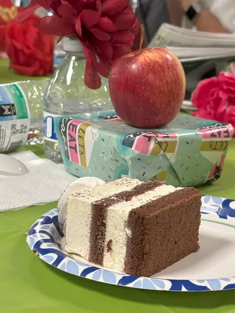 Close-up of birthday cake, an apple, and flower decorations on the party table