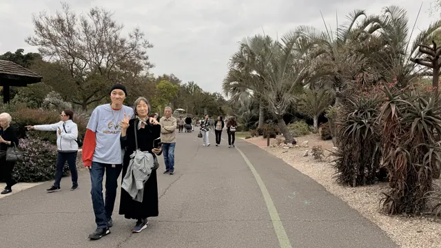 Two visitors posing on a path lined with palms and succulents