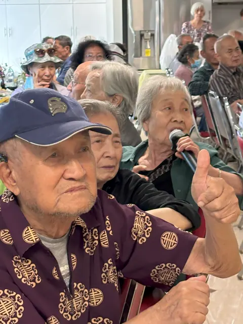 A resident shares a friendship story on the microphone as a neighbor gives a thumbs up