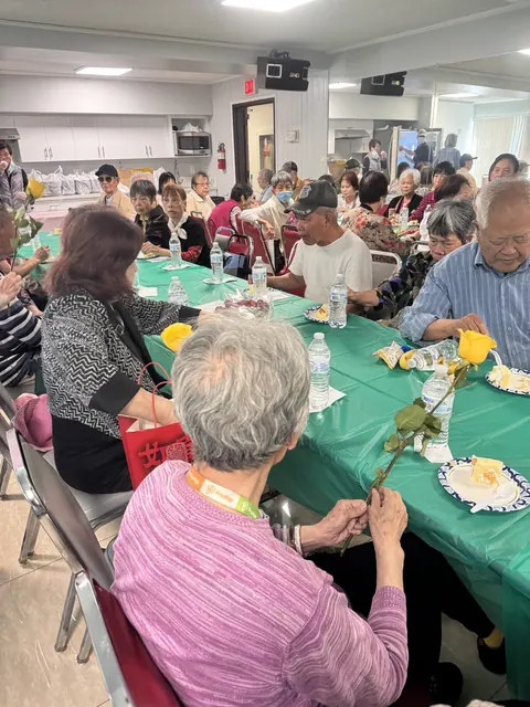 A resident admiring a yellow rose at the table, with cake and refreshments nearby